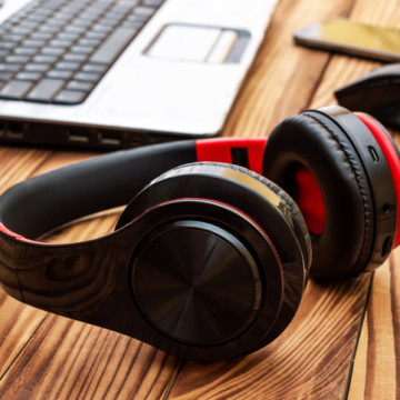 Headphones with laptop, computer mouse and smartphone on wooden desk. Close up.